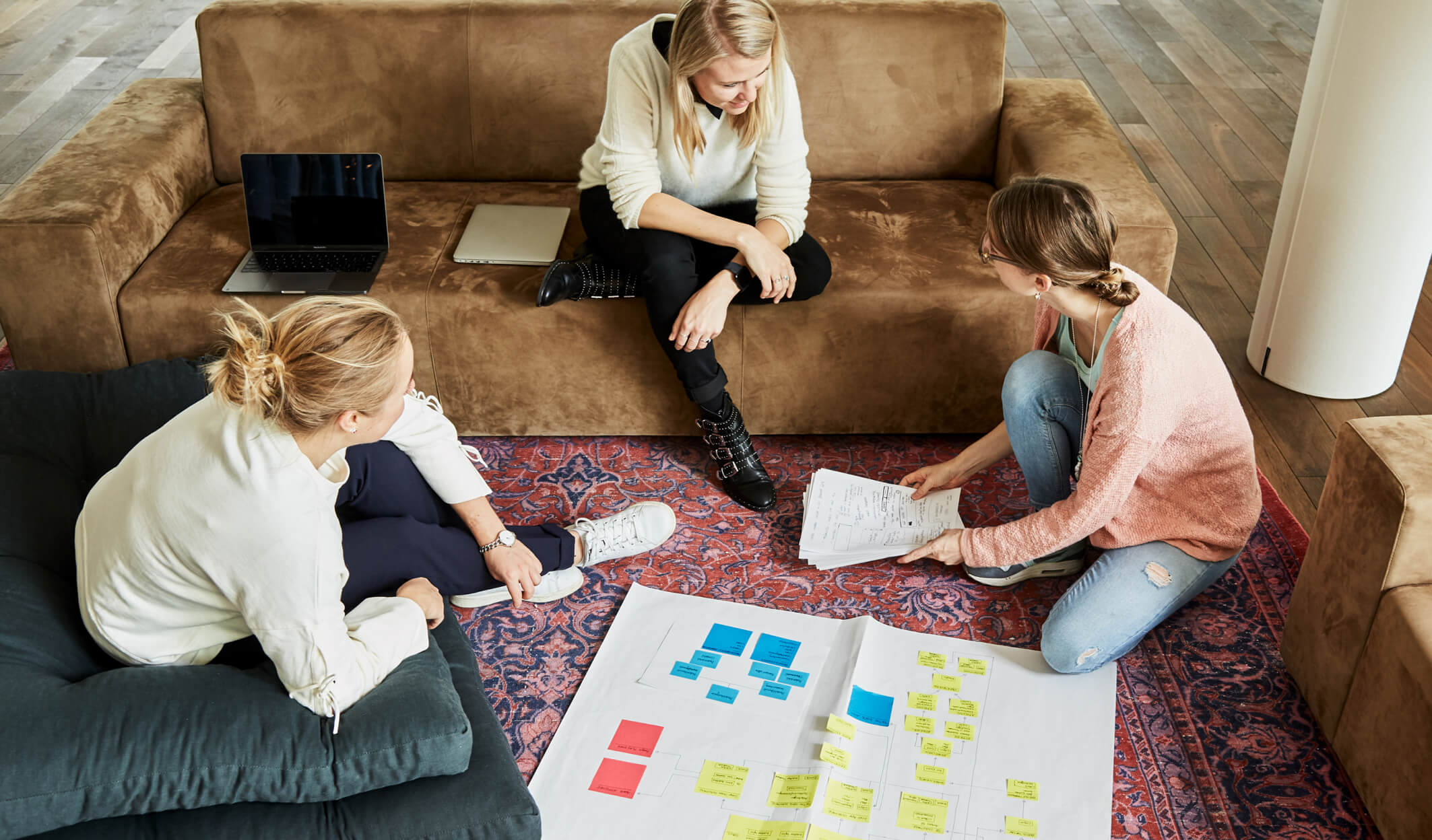 Ginetta Workspace members engaged in a brainstorming session on a sofa at Ginetta Workspace, surrounded by plans, sketches, and sticky notes, illustrating the collaborative and dynamic work environment.